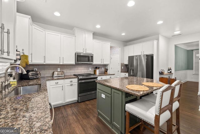 kitchen with dark wood-style floors, appliances with stainless steel finishes, white cabinetry, a sink, and dark stone countertops