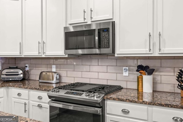 kitchen featuring stainless steel appliances, dark stone counters, white cabinetry, and backsplash