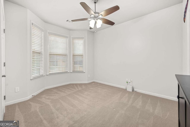 spare room featuring light carpet, ceiling fan, visible vents, and baseboards