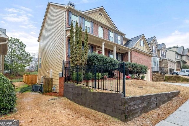 view of front of property featuring a residential view, central AC, fence, and brick siding