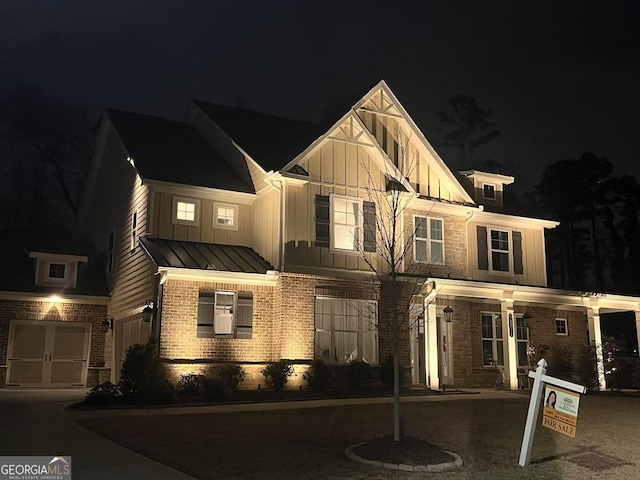 view of front facade featuring a standing seam roof, a garage, board and batten siding, brick siding, and metal roof