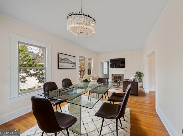 dining room featuring a chandelier, a brick fireplace, light wood-style flooring, and crown molding