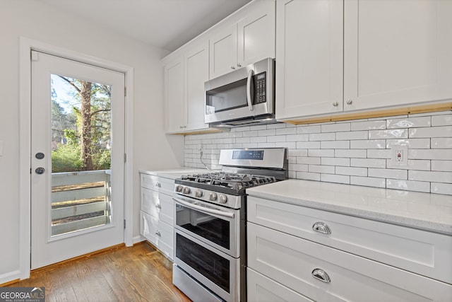 kitchen featuring light stone counters, light hardwood / wood-style flooring, white cabinets, stainless steel appliances, and backsplash