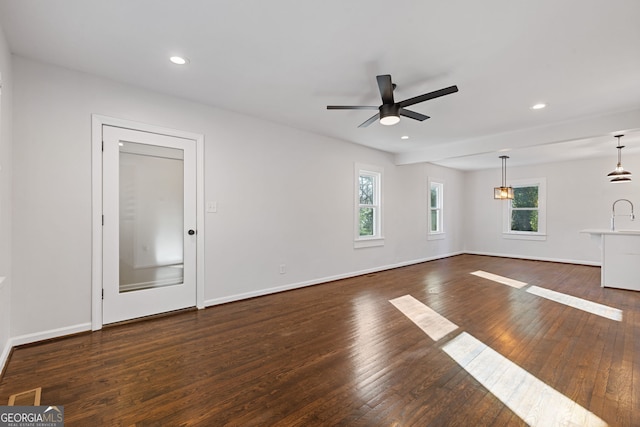 unfurnished living room featuring a wealth of natural light, dark wood-type flooring, and ceiling fan