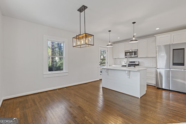 kitchen with white cabinetry, appliances with stainless steel finishes, an island with sink, and decorative light fixtures