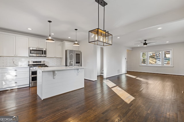 kitchen featuring white cabinetry, appliances with stainless steel finishes, hanging light fixtures, and a center island with sink