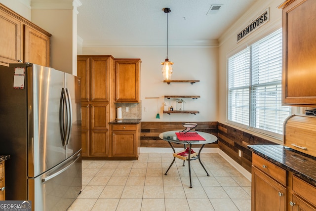 kitchen with pendant lighting, crown molding, stainless steel refrigerator, and wood walls