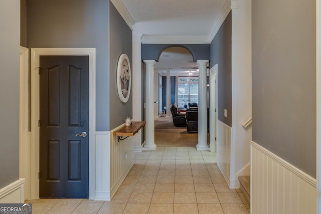 hall featuring light tile patterned floors, ornamental molding, a textured ceiling, and ornate columns