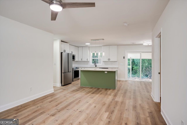 kitchen with a kitchen island, light countertops, appliances with stainless steel finishes, white cabinetry, and a sink