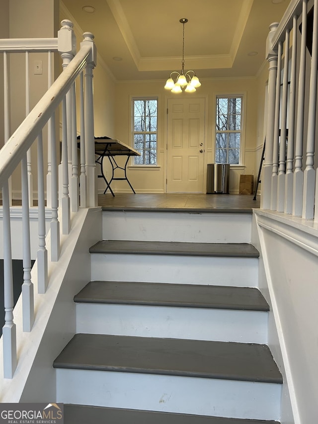 staircase with a tray ceiling, ornamental molding, and a chandelier