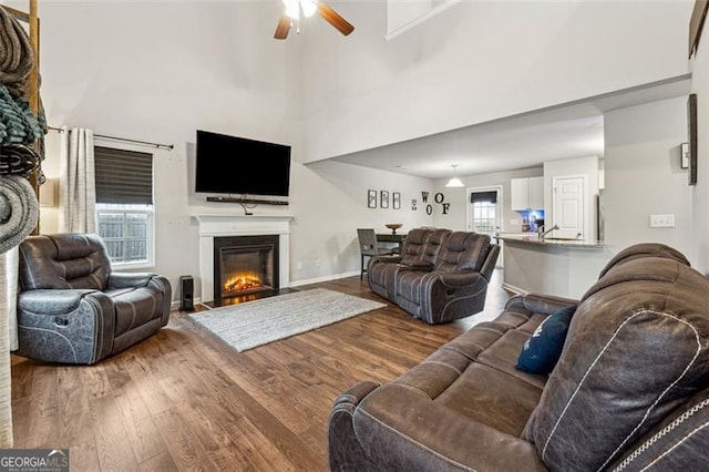 living room with hardwood / wood-style flooring, ceiling fan, sink, and a towering ceiling