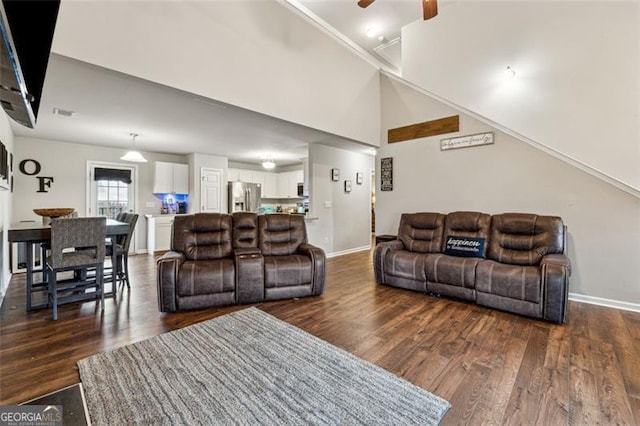 living room with dark wood-type flooring, ceiling fan, and a towering ceiling