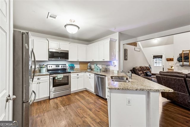 kitchen with sink, appliances with stainless steel finishes, kitchen peninsula, light stone countertops, and white cabinets