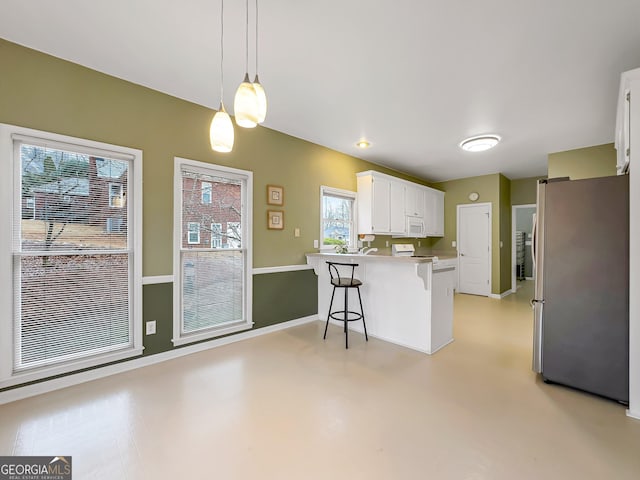 kitchen with a breakfast bar, stainless steel fridge, kitchen peninsula, pendant lighting, and white cabinets