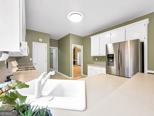 kitchen featuring stainless steel refrigerator with ice dispenser, stove, sink, and white cabinets