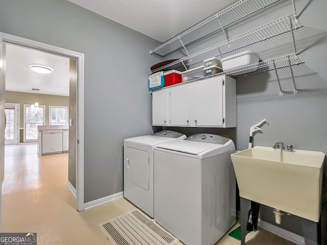 laundry room with sink, cabinets, a textured ceiling, light wood-type flooring, and washer and clothes dryer