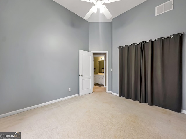 unfurnished bedroom with ceiling fan, light colored carpet, and a towering ceiling