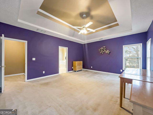 interior space with ceiling fan, ensuite bathroom, a tray ceiling, and light carpet