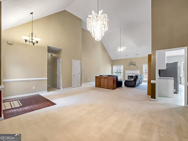 unfurnished living room with carpet flooring, ceiling fan with notable chandelier, and high vaulted ceiling