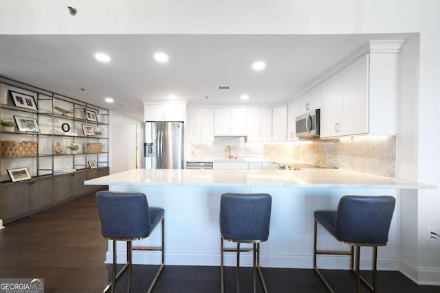 kitchen with white cabinetry, a breakfast bar area, kitchen peninsula, and appliances with stainless steel finishes