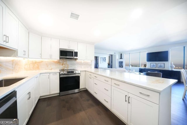 kitchen featuring white cabinetry, dark hardwood / wood-style floors, kitchen peninsula, stainless steel appliances, and backsplash