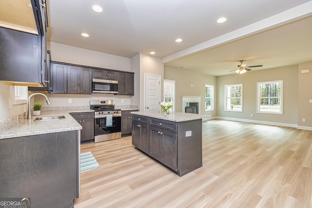 kitchen with a kitchen island, appliances with stainless steel finishes, sink, light stone counters, and light hardwood / wood-style floors