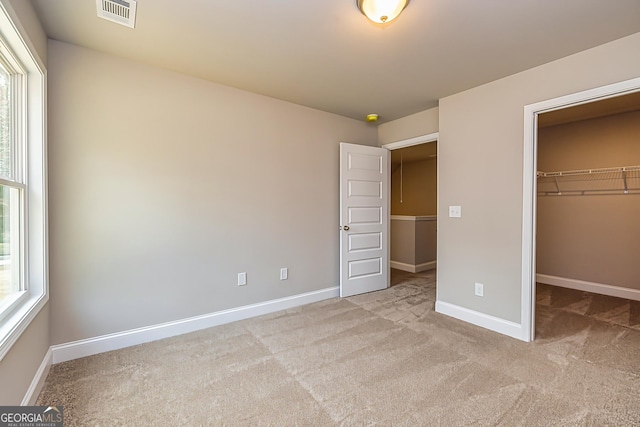 unfurnished bedroom featuring light colored carpet, a closet, multiple windows, and a walk in closet