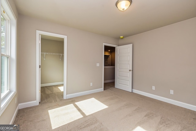 unfurnished bedroom with multiple windows, a spacious closet, light colored carpet, and a closet