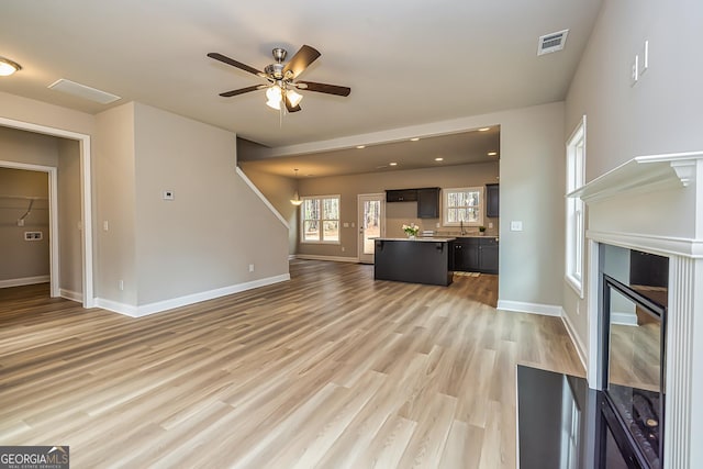 unfurnished living room featuring ceiling fan, sink, and light wood-type flooring