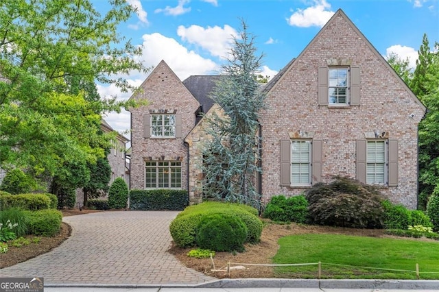 view of front of property featuring brick siding, decorative driveway, and a front lawn