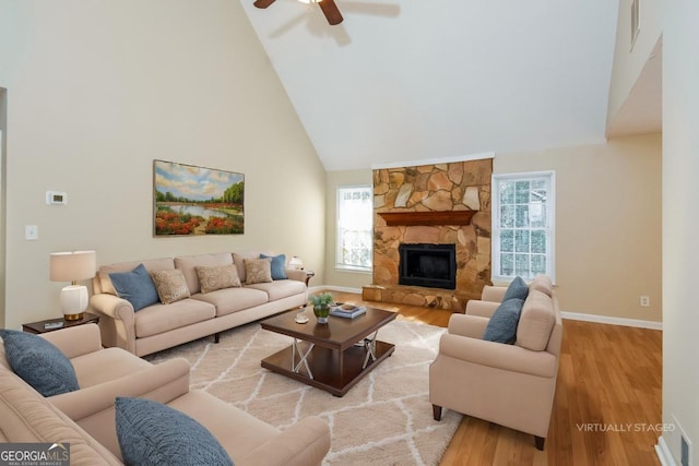 living room with high vaulted ceiling, a wealth of natural light, a stone fireplace, and light hardwood / wood-style floors