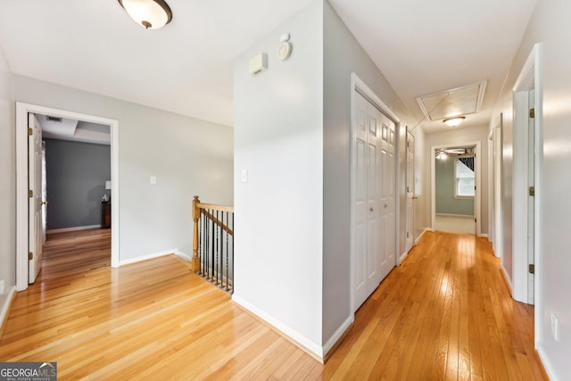 corridor featuring attic access, baseboards, light wood finished floors, and an upstairs landing