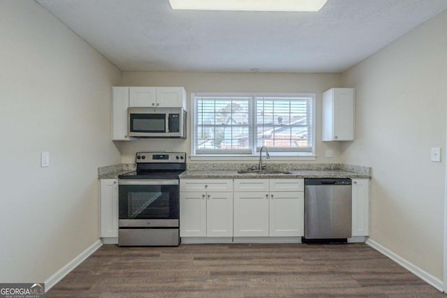 kitchen featuring sink, hardwood / wood-style flooring, stainless steel appliances, light stone countertops, and white cabinets