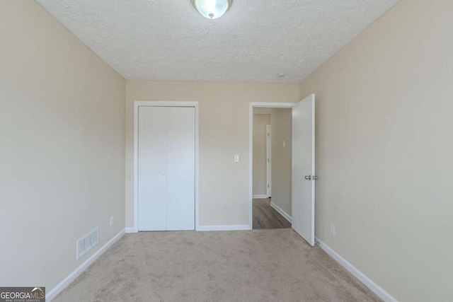 unfurnished bedroom featuring light carpet, a textured ceiling, and a closet