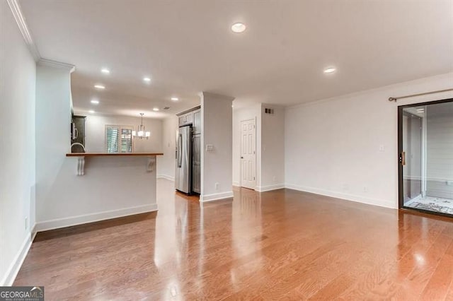 unfurnished living room with an inviting chandelier, hardwood / wood-style floors, and ornamental molding