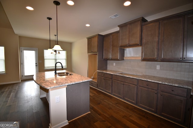 kitchen with a kitchen island with sink, a sink, dark wood-style flooring, visible vents, and backsplash