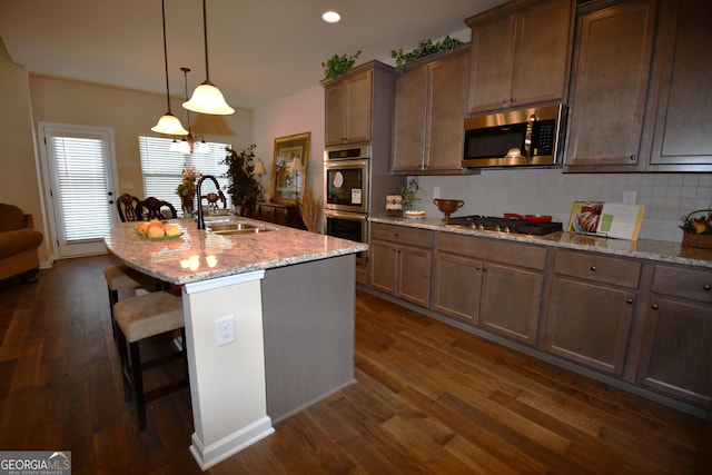 kitchen featuring a sink, a kitchen bar, appliances with stainless steel finishes, light stone countertops, and dark wood-style floors