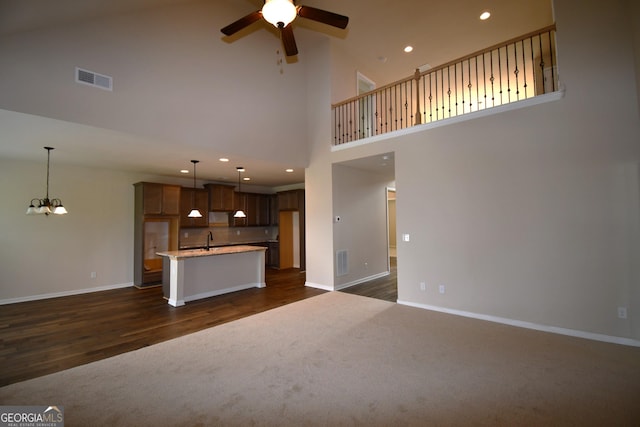 unfurnished living room featuring visible vents, a towering ceiling, a sink, and ceiling fan with notable chandelier