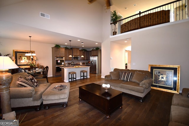 living area with visible vents, dark wood-style floors, a high ceiling, and a chandelier