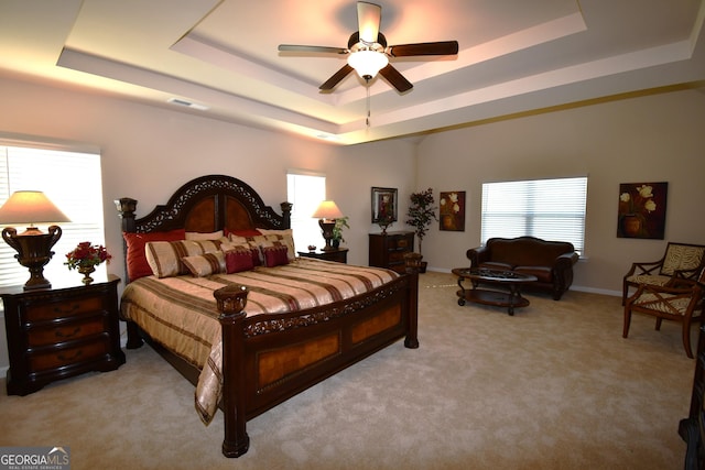 bedroom featuring ceiling fan, light carpet, a tray ceiling, baseboards, and visible vents