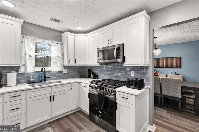 kitchen featuring appliances with stainless steel finishes, tasteful backsplash, sink, white cabinets, and dark wood-type flooring