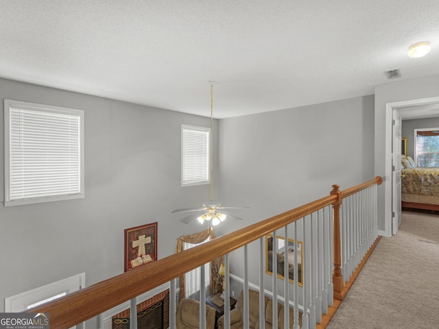 hallway with a textured ceiling, visible vents, an upstairs landing, baseboards, and carpet