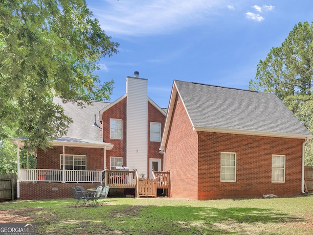 rear view of house featuring a shingled roof, brick siding, a yard, a wooden deck, and a chimney