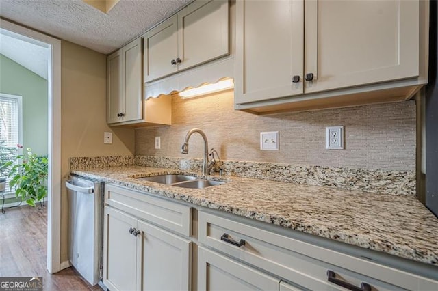 kitchen featuring light stone counters, stainless steel dishwasher, sink, and white cabinets