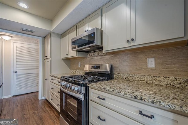 kitchen with dark wood-type flooring, white cabinetry, light stone counters, stainless steel appliances, and decorative backsplash