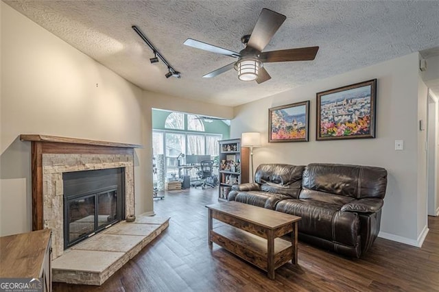 living room featuring rail lighting, a stone fireplace, dark hardwood / wood-style floors, and a textured ceiling