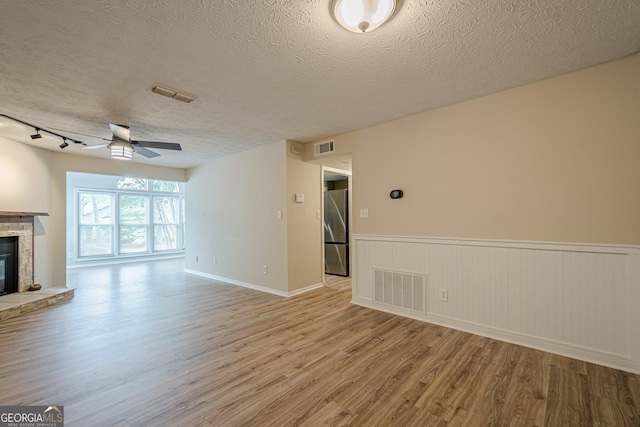 3205 Canyon Point Cir, Roswell, GA 30076 - unfurnished living room with a textured ceiling, a stone fireplace, a ceiling fan, wood finished floors, and wainscoting