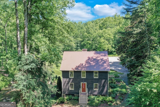 colonial inspired home with a forest view, metal roof, and a chimney