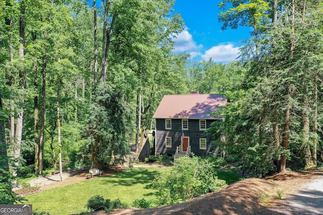 colonial inspired home featuring metal roof, a chimney, a front yard, and a forest view