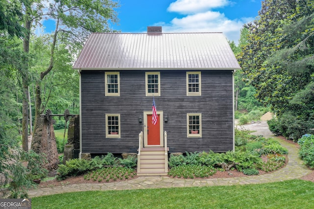 colonial inspired home featuring entry steps, metal roof, a front lawn, and a chimney